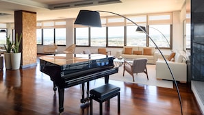 A spacious living room with a grand piano, a modern lamp, and a large window offering a city view. - Melia Castelo Branco (Castelo Branco)
