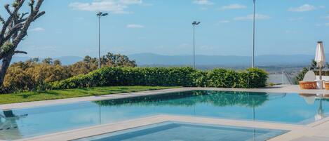 A clear swimming pool with a view of distant mountains, surrounded by greenery and outdoor furniture.