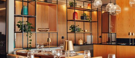 Un comedor moderno con una mesa de madera dispuesta para una comida, rodeado de estantes con plantas y objetos decorativos.