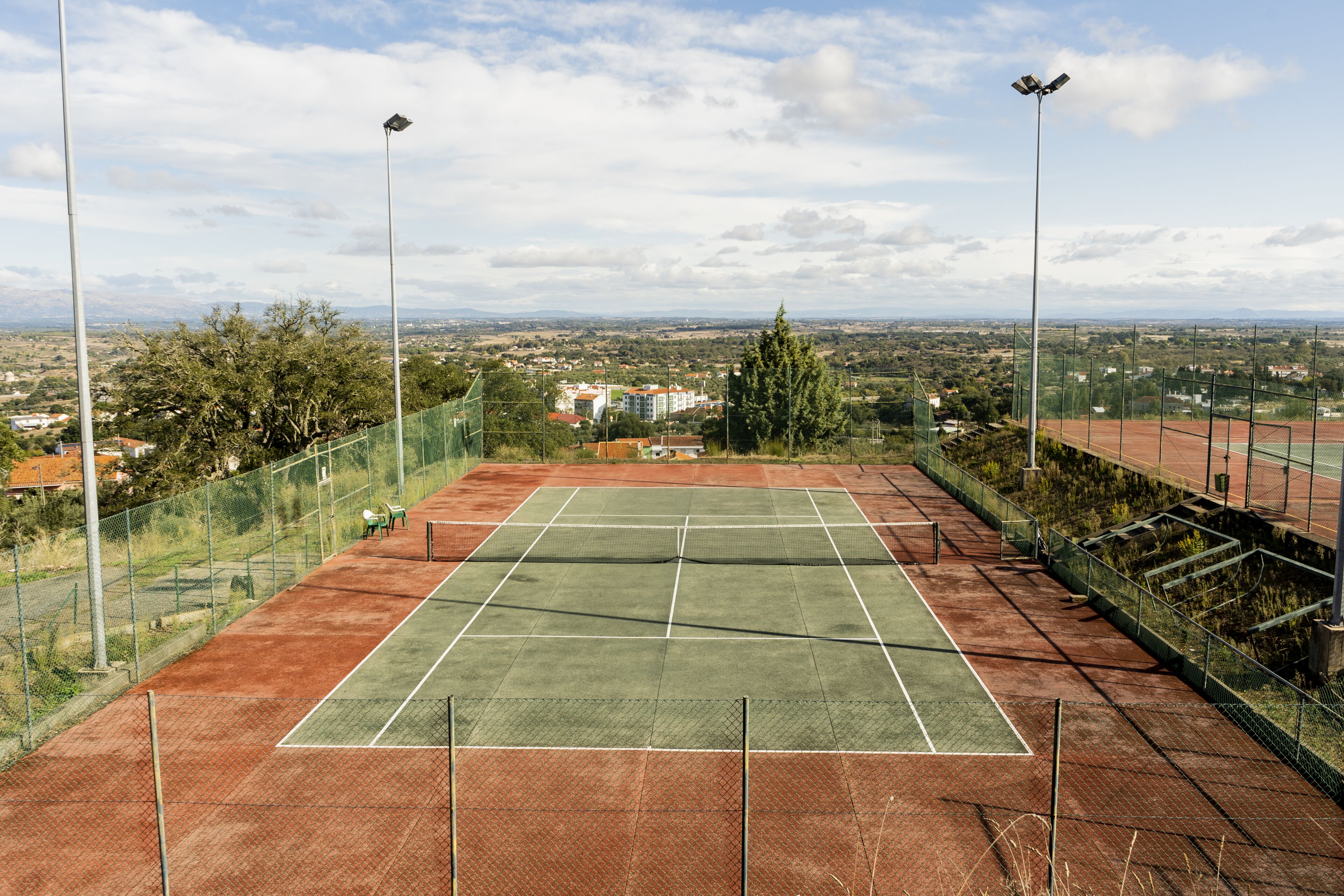 Un court de tennis avec un filet, entouré d’une clôture, et offrant une vue sur le paysage urbain.
