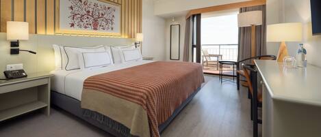 Une chambre d’hôtel comprenant un lit, des tables de chevet, un bureau, une chaise, un balcon et une grande fenêtre.