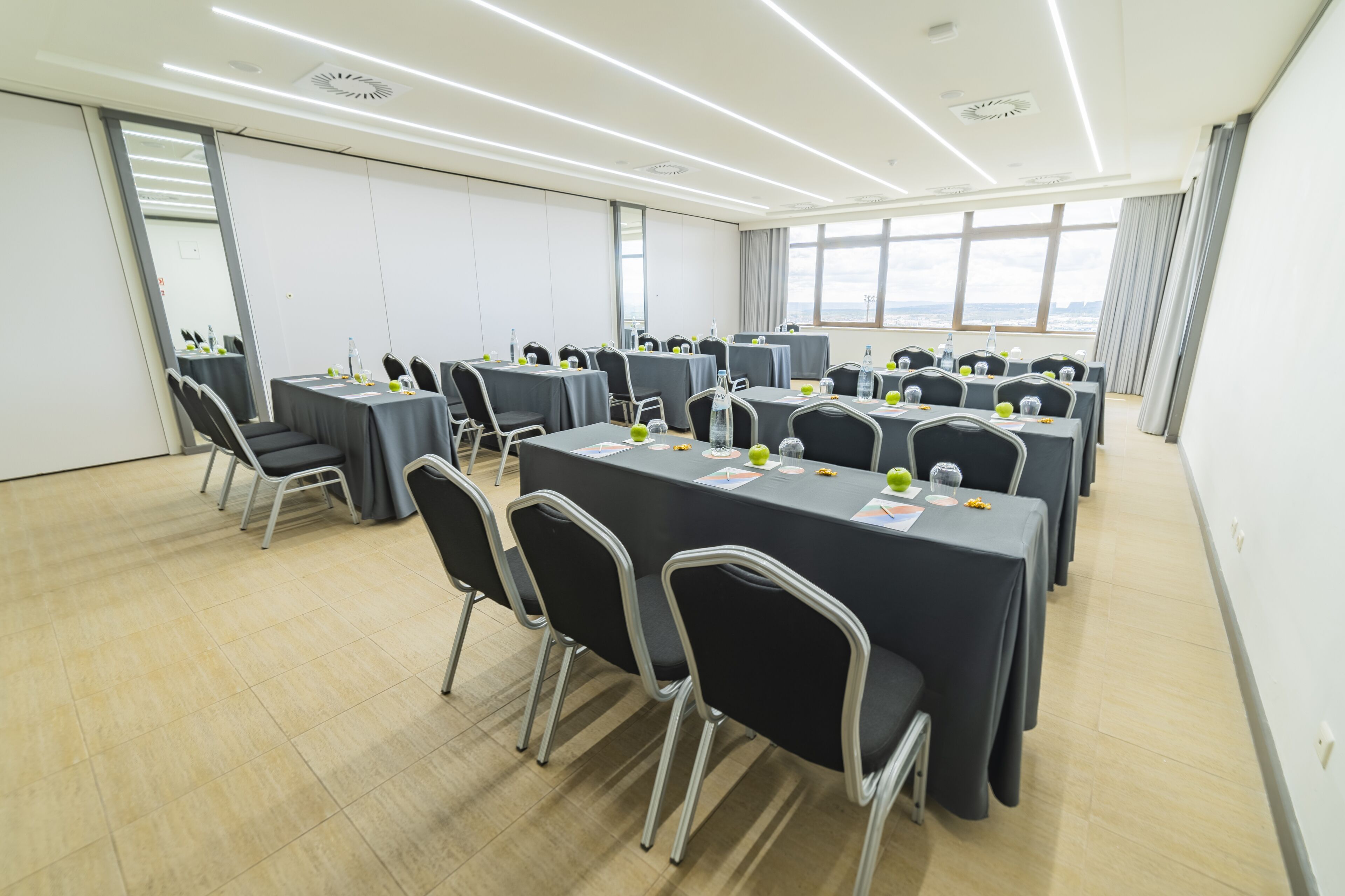 A conference room with multiple tables and chairs, large windows, and a view of the city.