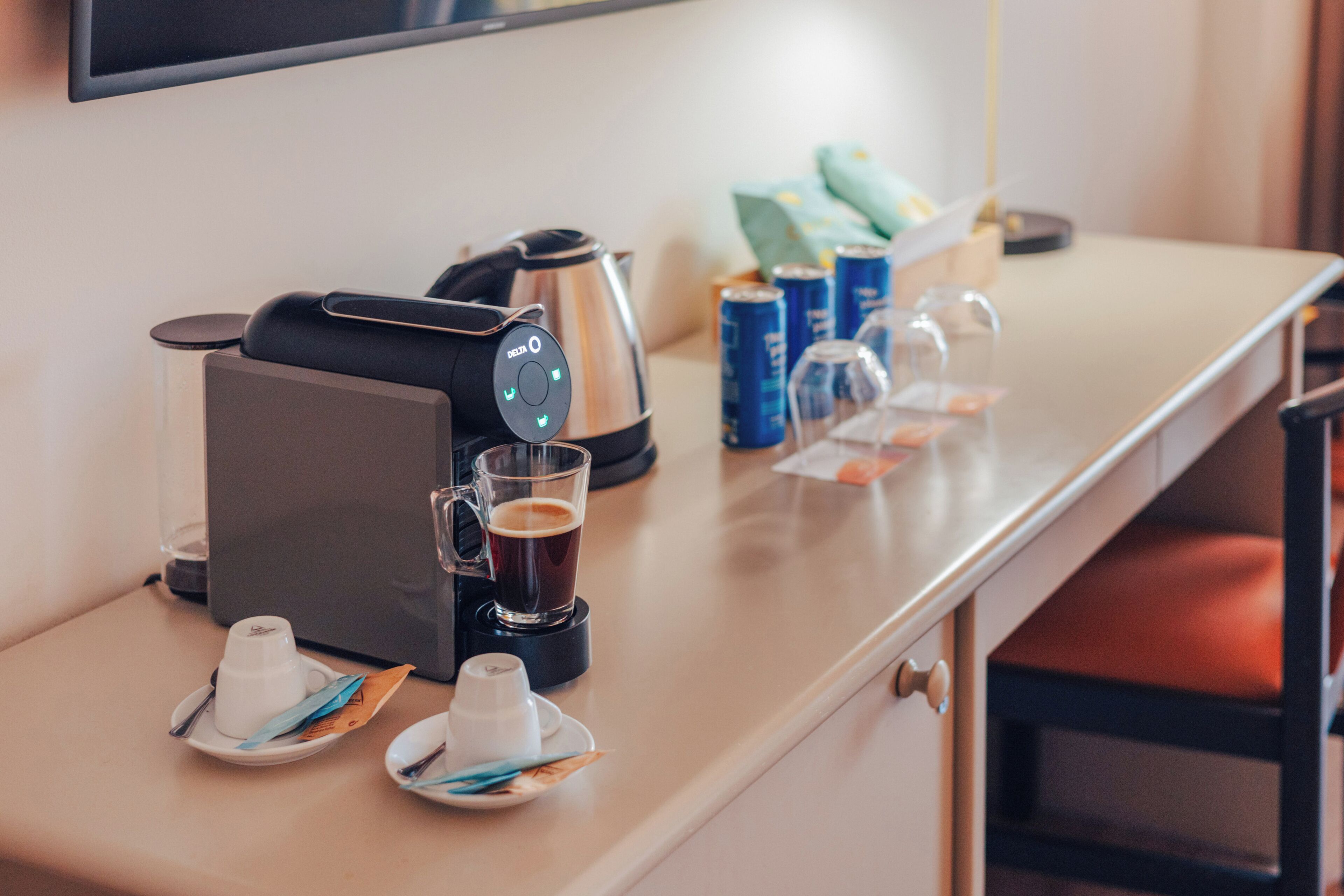 A hotel room with a coffee maker, a glass of coffee, tea cups, and a minibar.