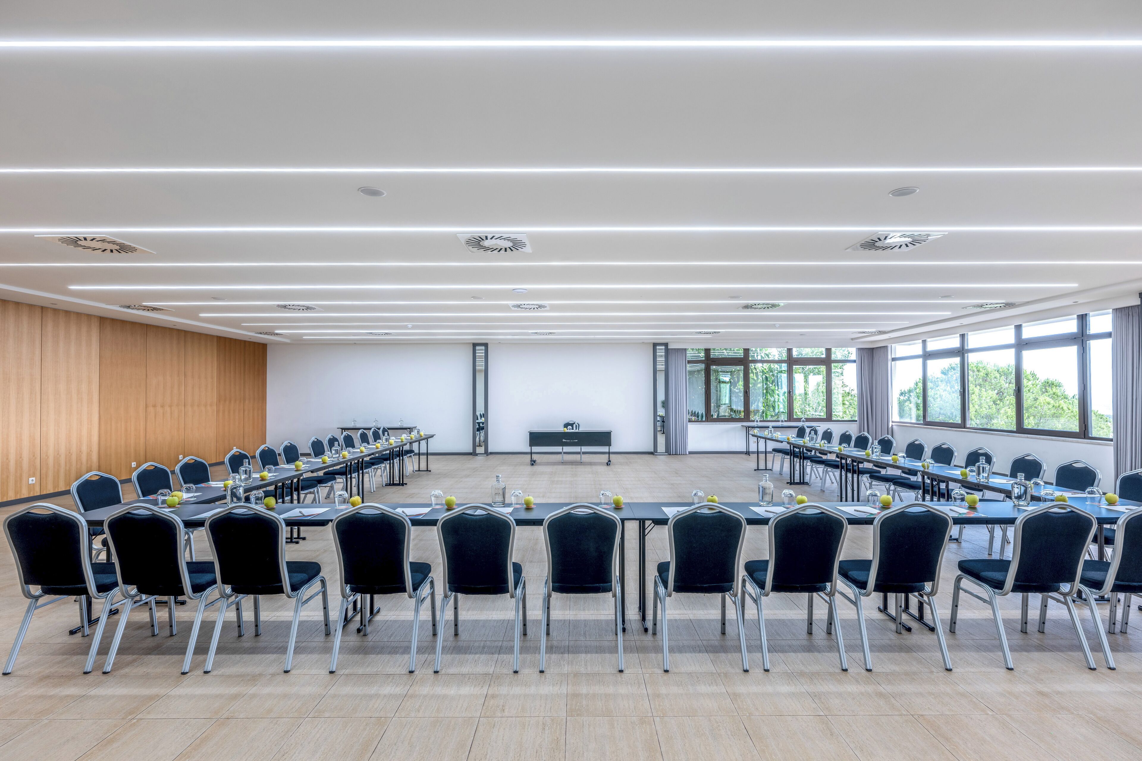 A conference room with multiple tables and chairs, large windows, and a wooden panel wall.
