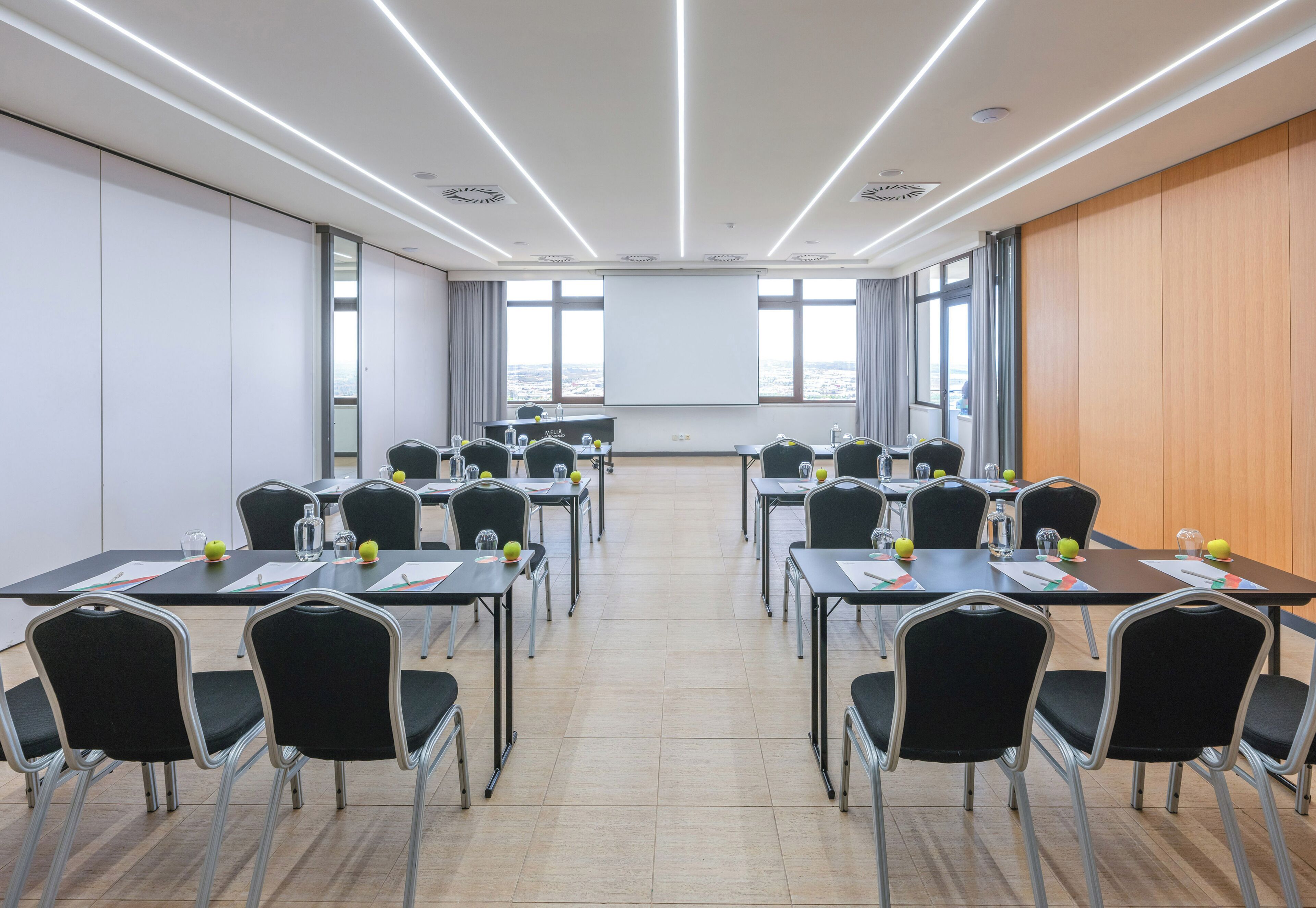 A conference room with a long table, chairs, a projector screen, and large windows.
