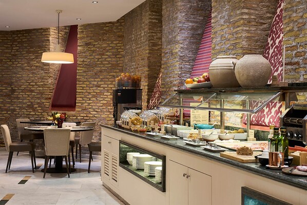 Un restaurante con pared de ladrillo, una mesa redonda con sillas y un mostrador de buffet con diversas opciones de comida.