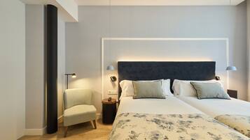 A modern hotel room with a large bed, two bedside tables, a chair, and a wall-mounted telephone.