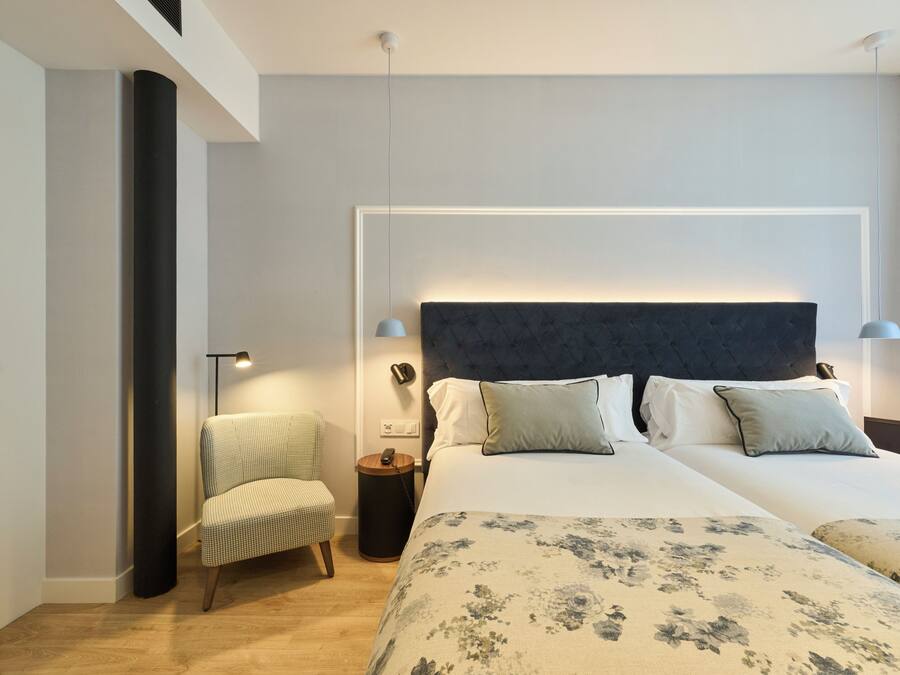 Una habitación de hotel moderna con una cama grande, dos mesitas de noche, una silla y un teléfono instalado en la pared.