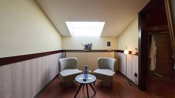 Habitación de hotel con tragaluz, dos sillas de mimbre, una mesita con una botella y un teléfono, y una lámpara de noche.