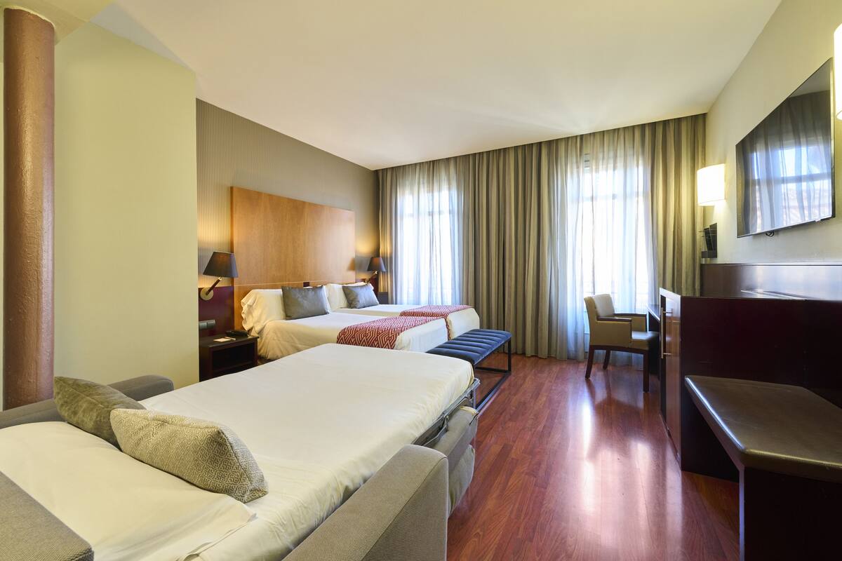 A hotel room with two beds, a desk, a chair, and a TV.