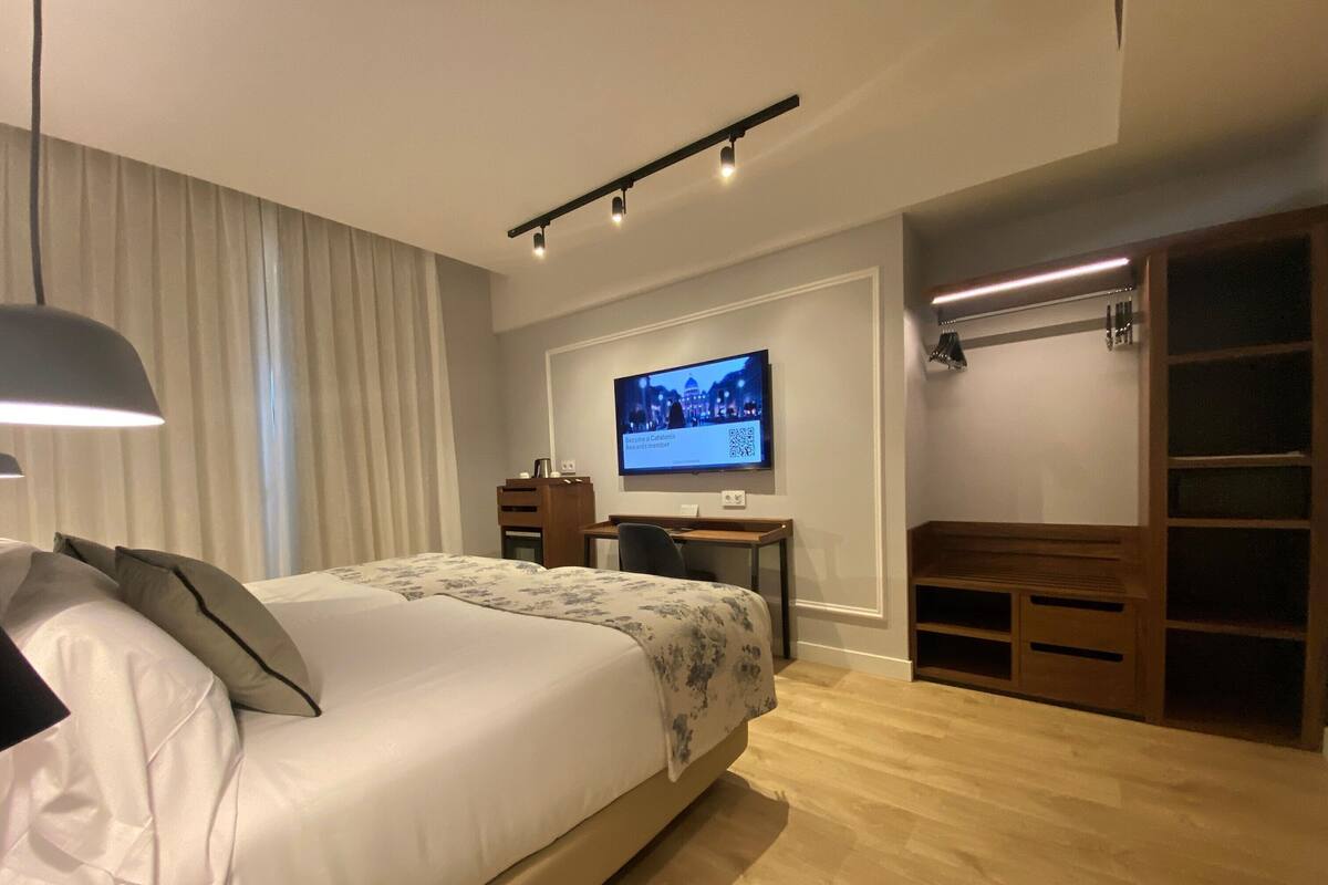 A modern hotel room with a bed, a desk, a television, and a wardrobe.