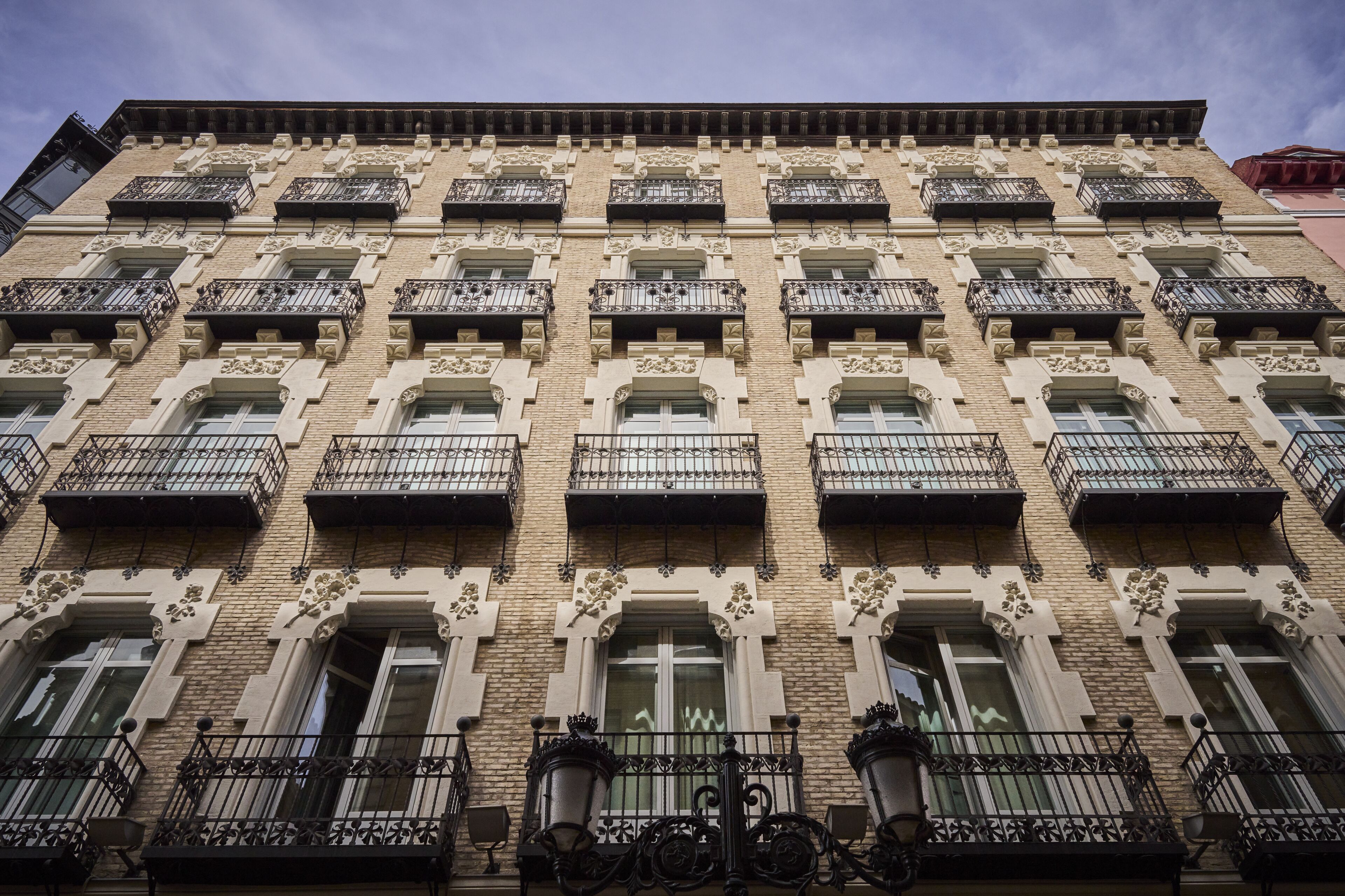 Ein mehrgeschossiges Gebäude mit einheitlicher Fassade, gekennzeichnet durch gleichmäßig angeordnete Fenster und Balkone mit aufwendig gestalteten Metallgeländern.