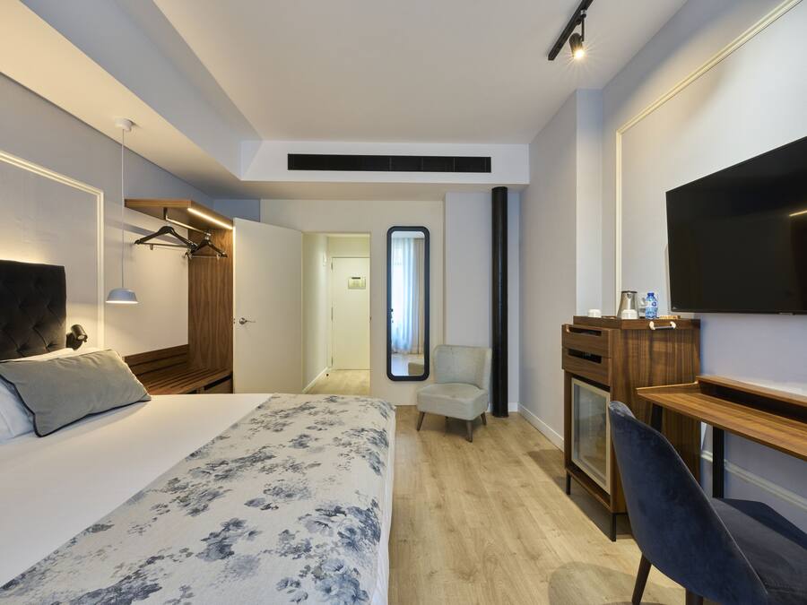 Ett hotellrum med en säng, ett skrivbord, en stol, en tv och en garderob.