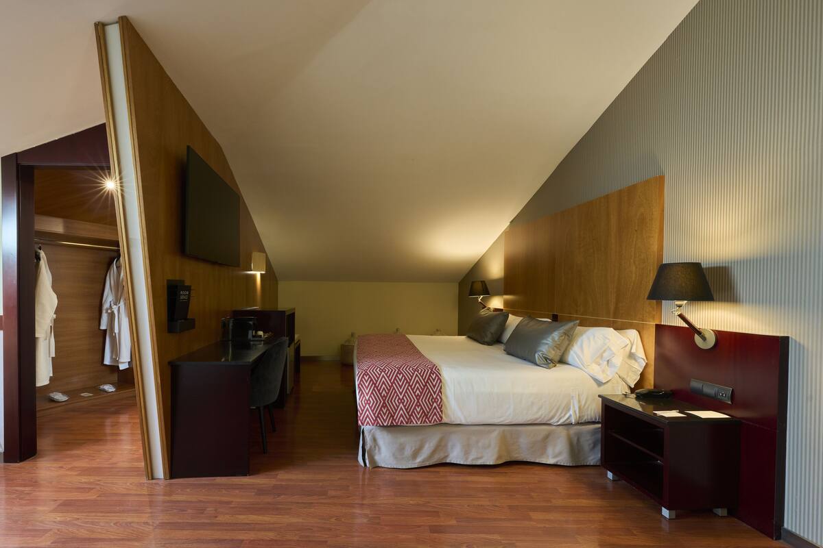 A hotel room with a bed, bedside table, lamp, and a desk with a chair.