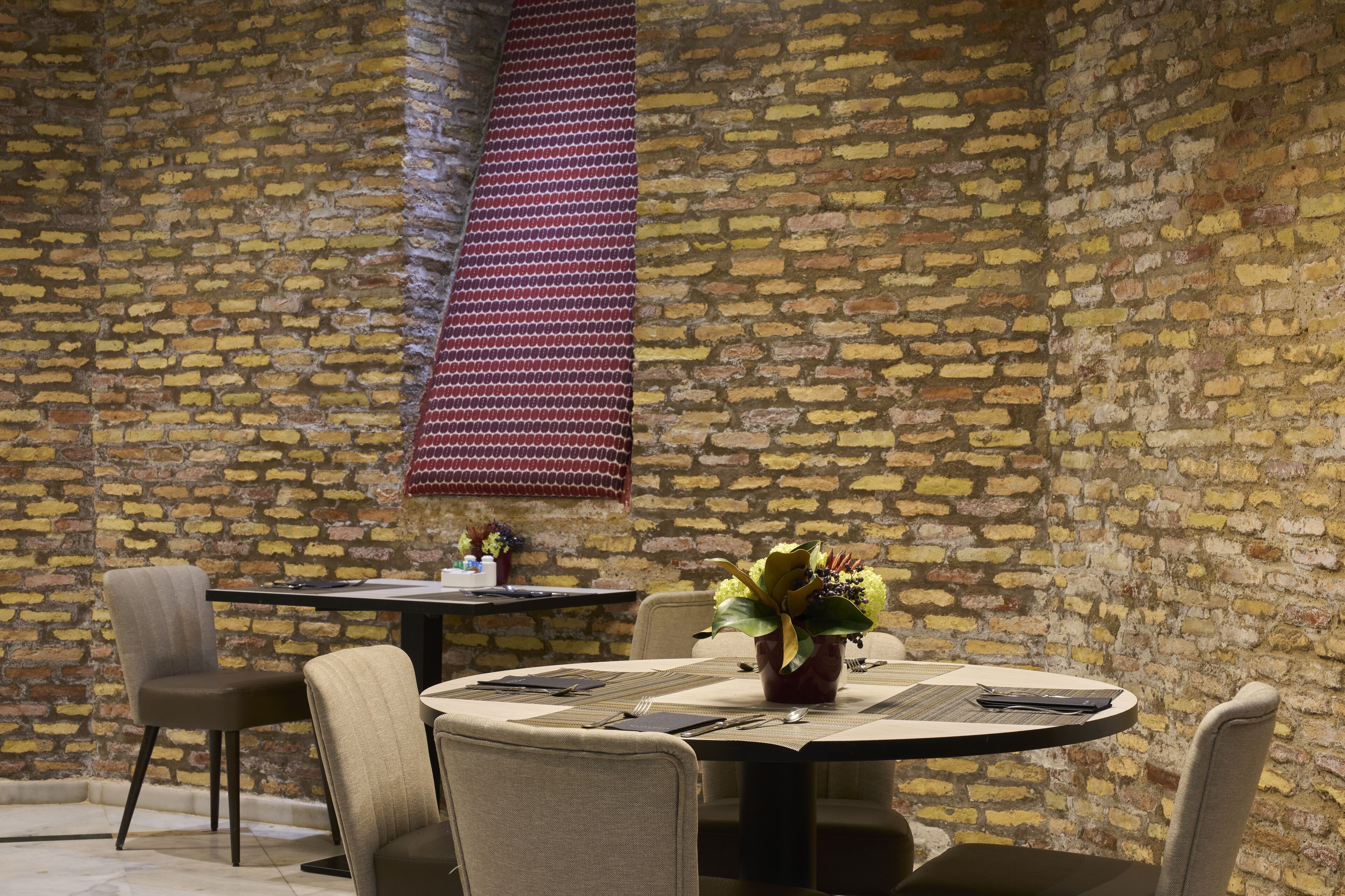 Un comedor con pared de ladrillo, una mesa redonda con un jarrón de flores y dos sillas.