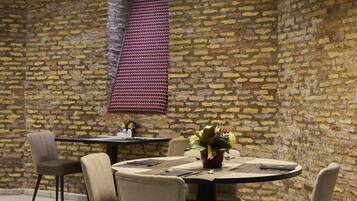 Un coin repas avec un mur en briques, une table ronde agrémentée d’un vase de fleurs et deux chaises.