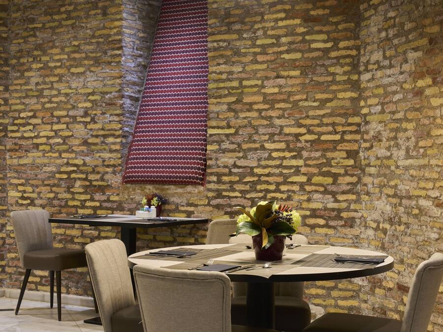A dining area with a brick wall, a round table set with a vase of flowers, and two chairs.