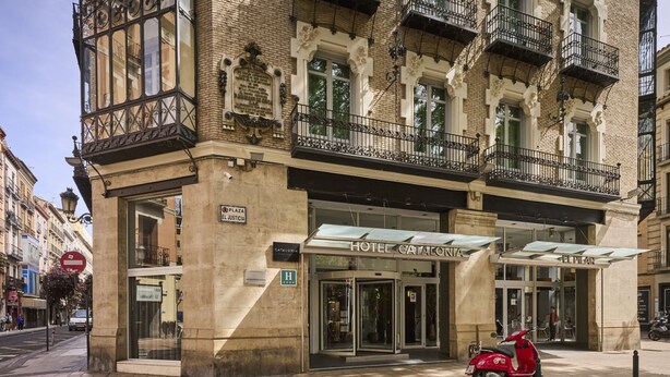 A historic building with a prominent entrance, a sign for 'Hotel Catalonia', and a red scooter parked outside. - Catalonia El Pilar (Zaragoza)