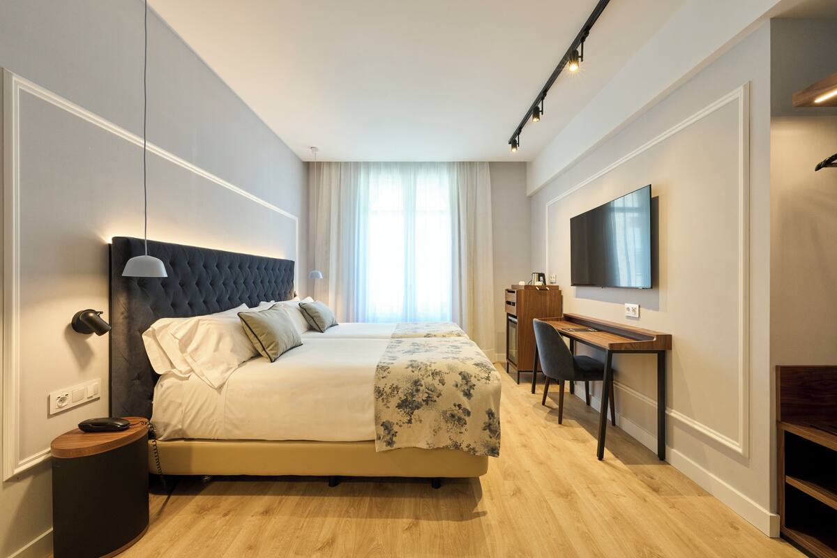 A hotel room with a large bed, a desk, a chair, a TV, and a bedside lamp.