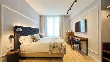 Habitación de hotel con una cama grande, un escritorio, una silla, un televisor y una lámpara de noche.