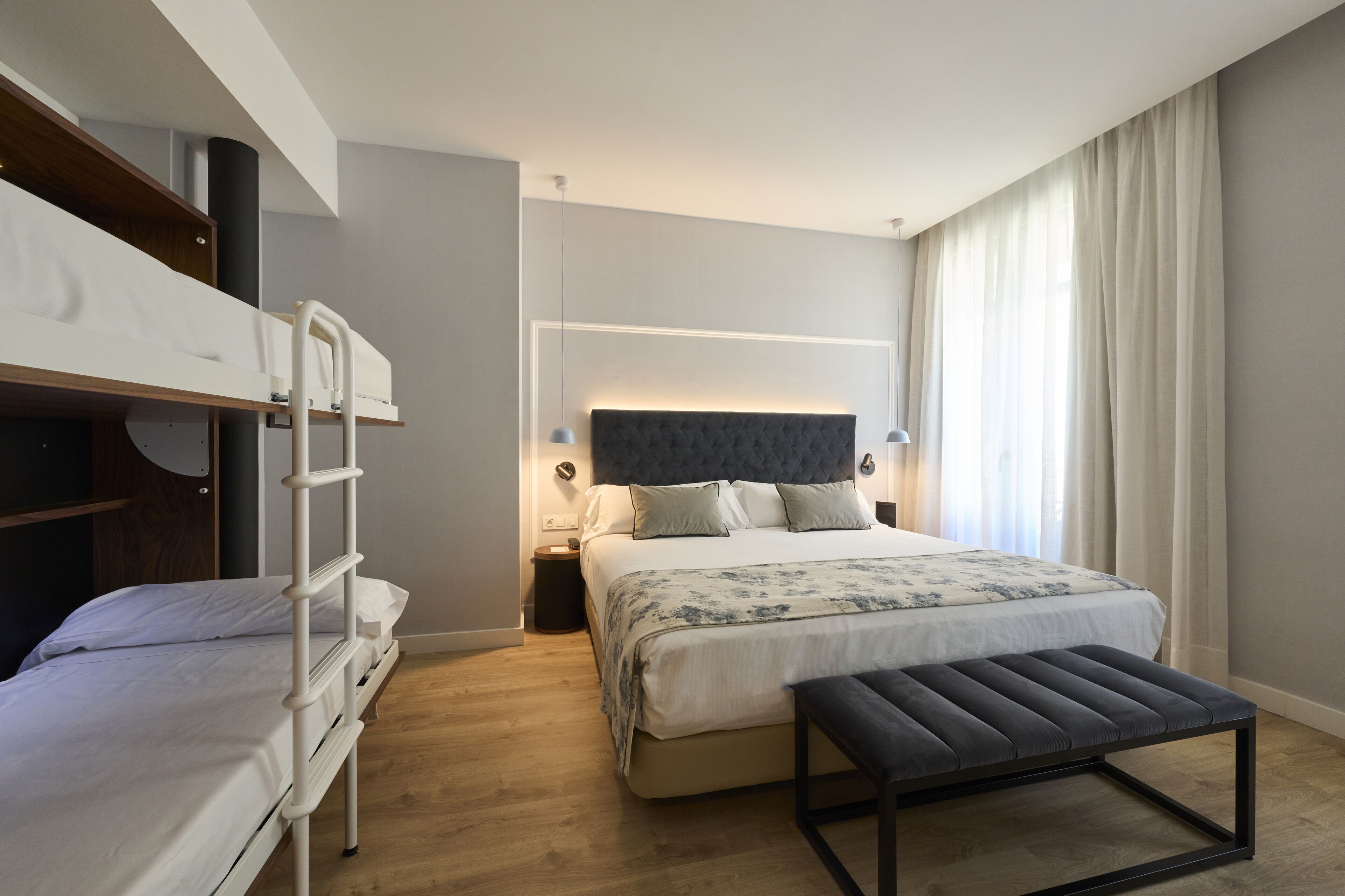 Un dormitorio moderno con una litera, una cama grande con cabecera y un banco.