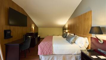 A hotel room with a bed, desk, chair, and a flat-screen TV mounted on the wall.