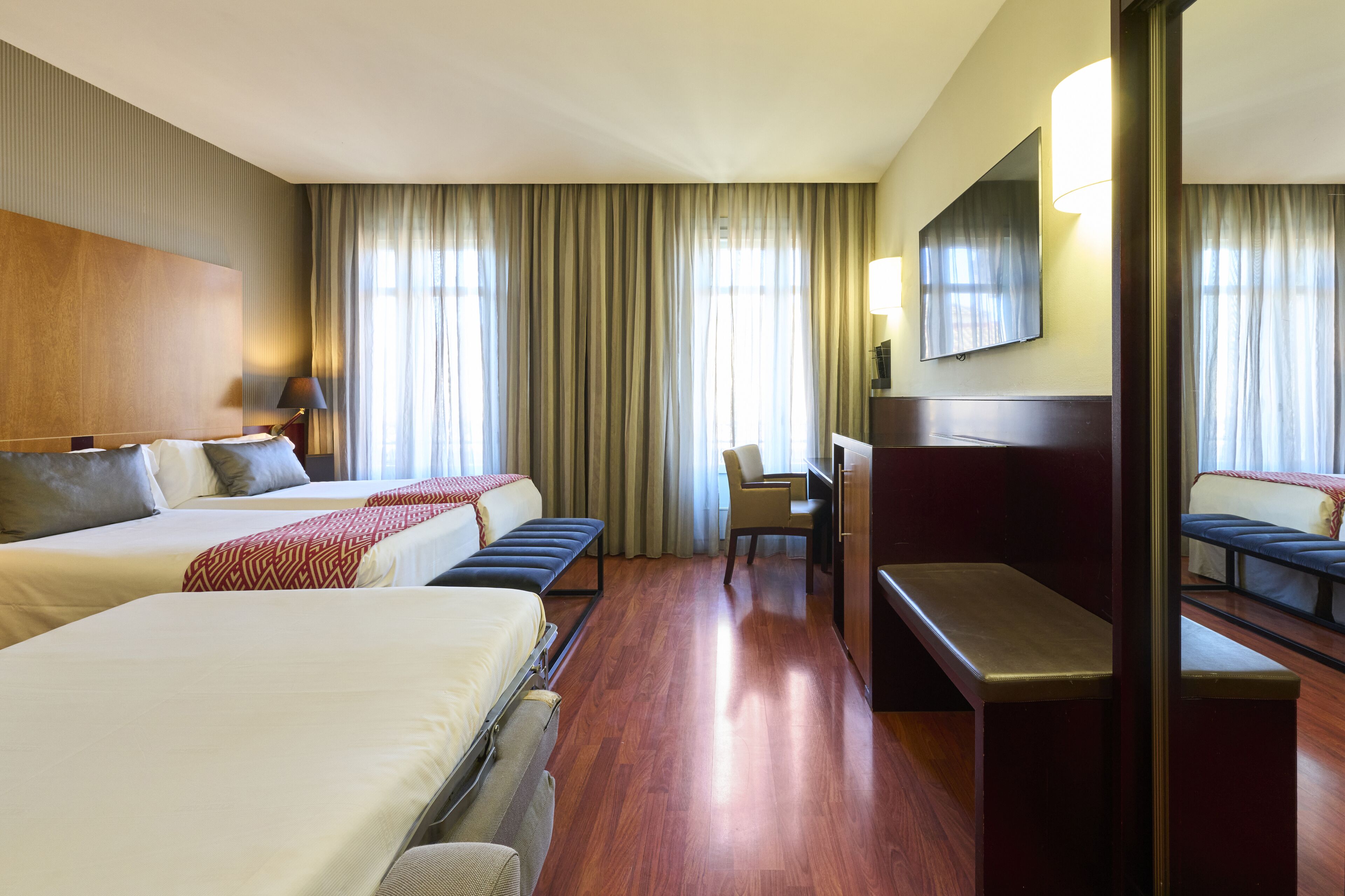 A hotel room with two beds, a desk, a chair, and a large mirror.