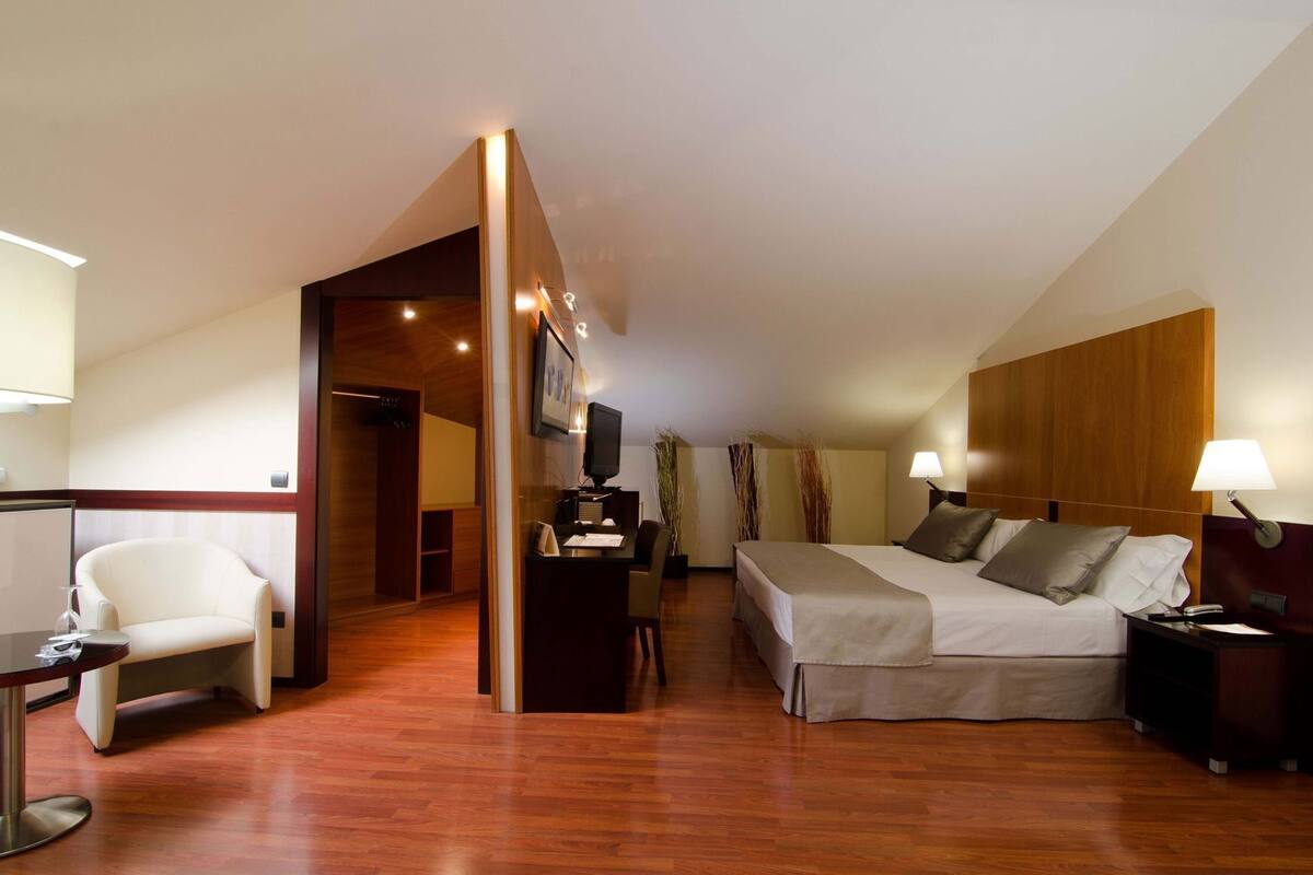 A hotel room with a bed, desk, chair, and a TV.