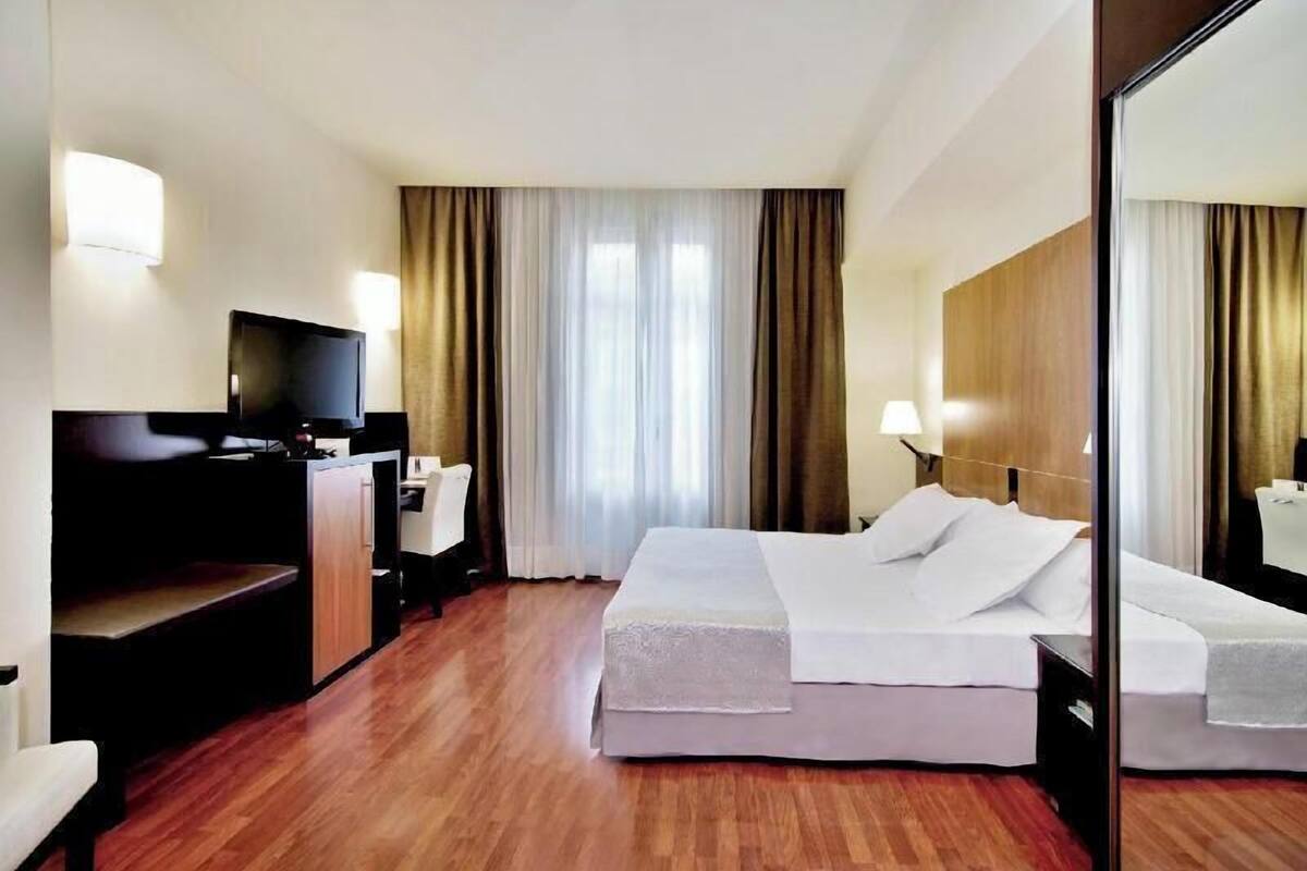 A hotel room with a bed, a desk with a computer, a television, and a large mirror.