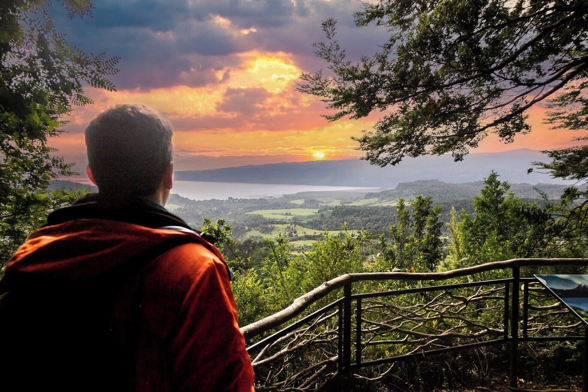 Uma pessoa contemplando uma paisagem deslumbrante, com vista para um corpo d'água e colinas.