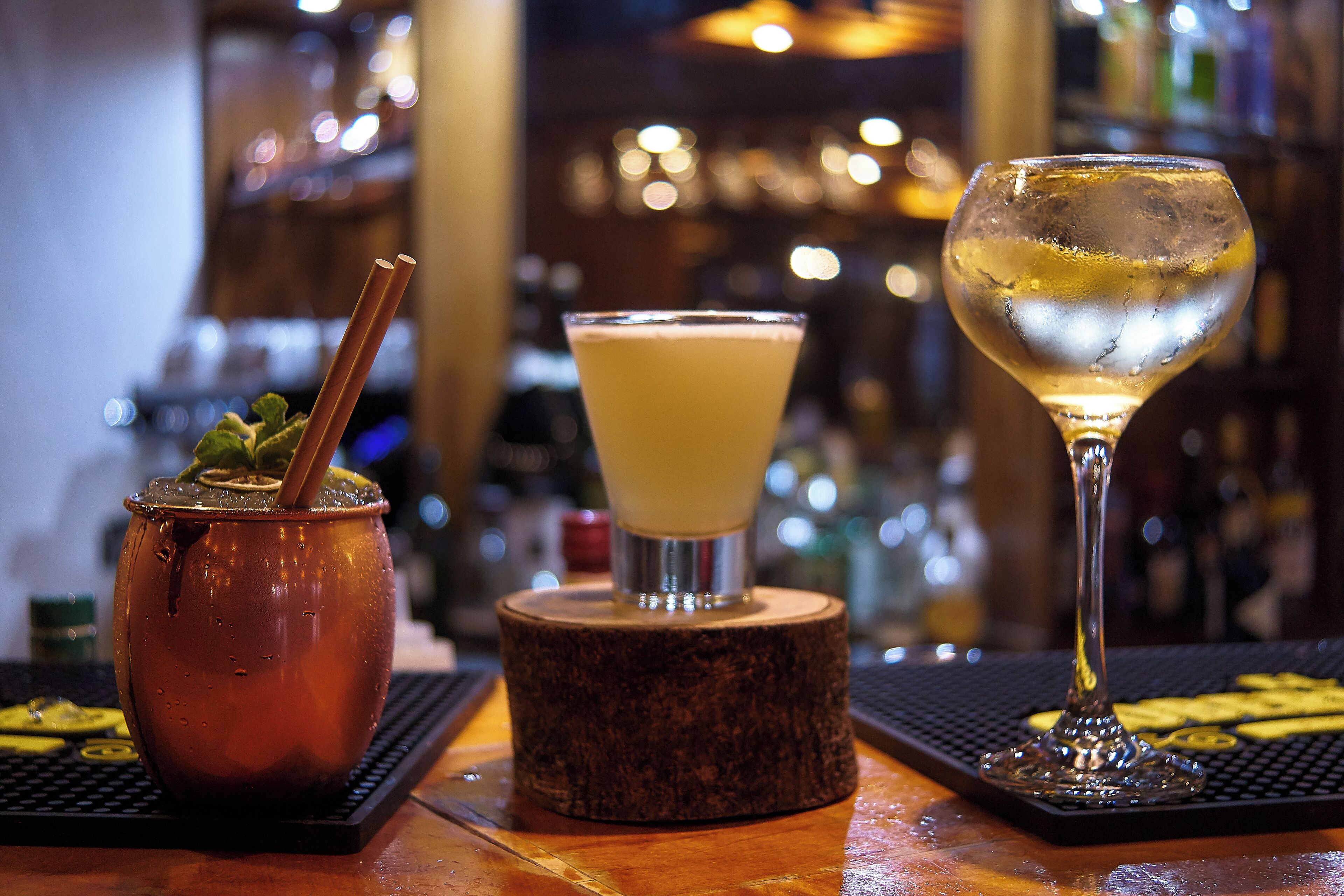 A bar setting with a traditional drink in a copper pot, a cocktail in a martini glass, and a glass of white wine.