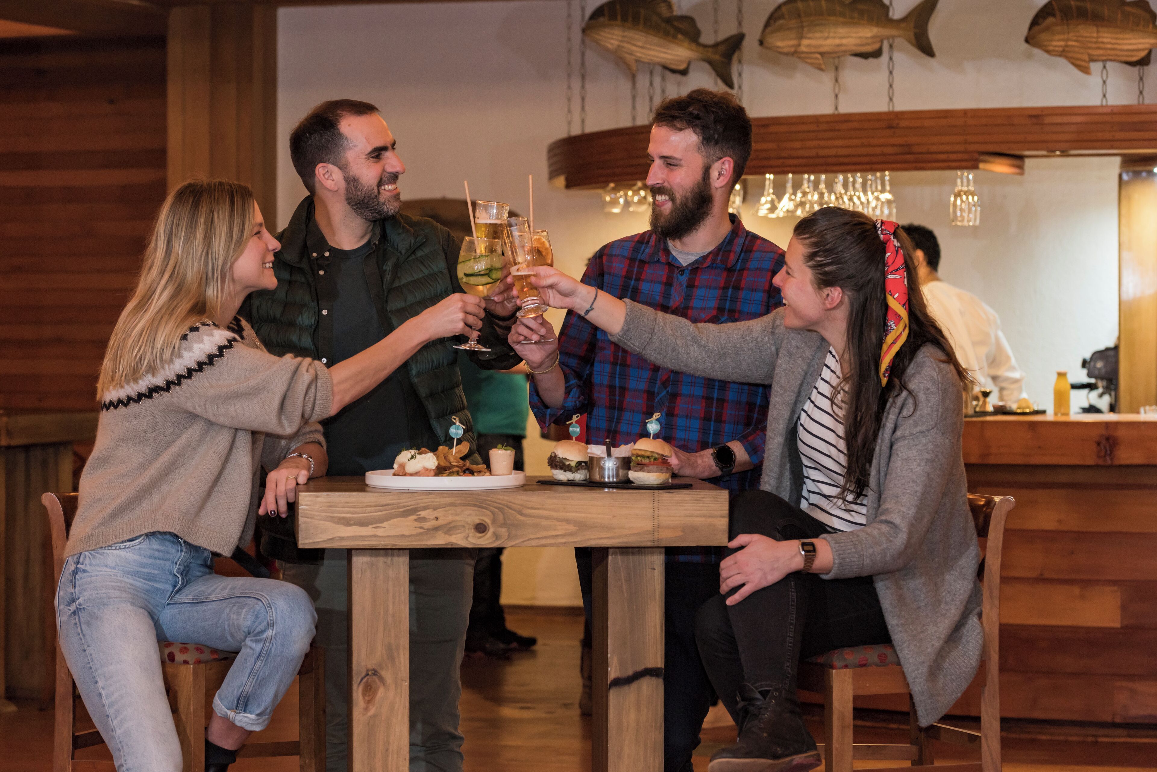 A group of people toasting at a wooden table in a restaurant with a rustic interior and fish-themed decor.