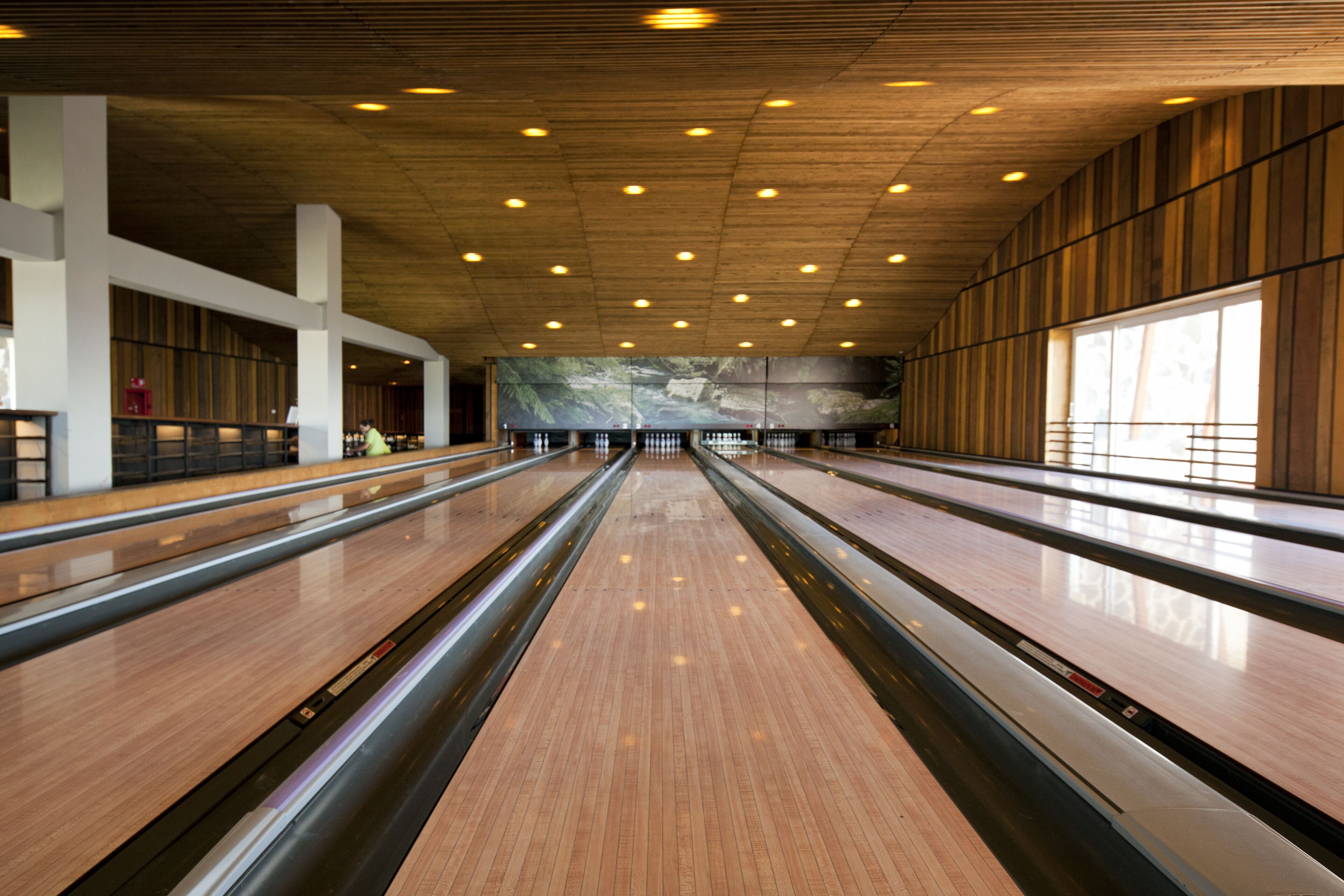 A bowling alley with multiple lanes, wooden floors, and a modern ceiling with recessed lighting.