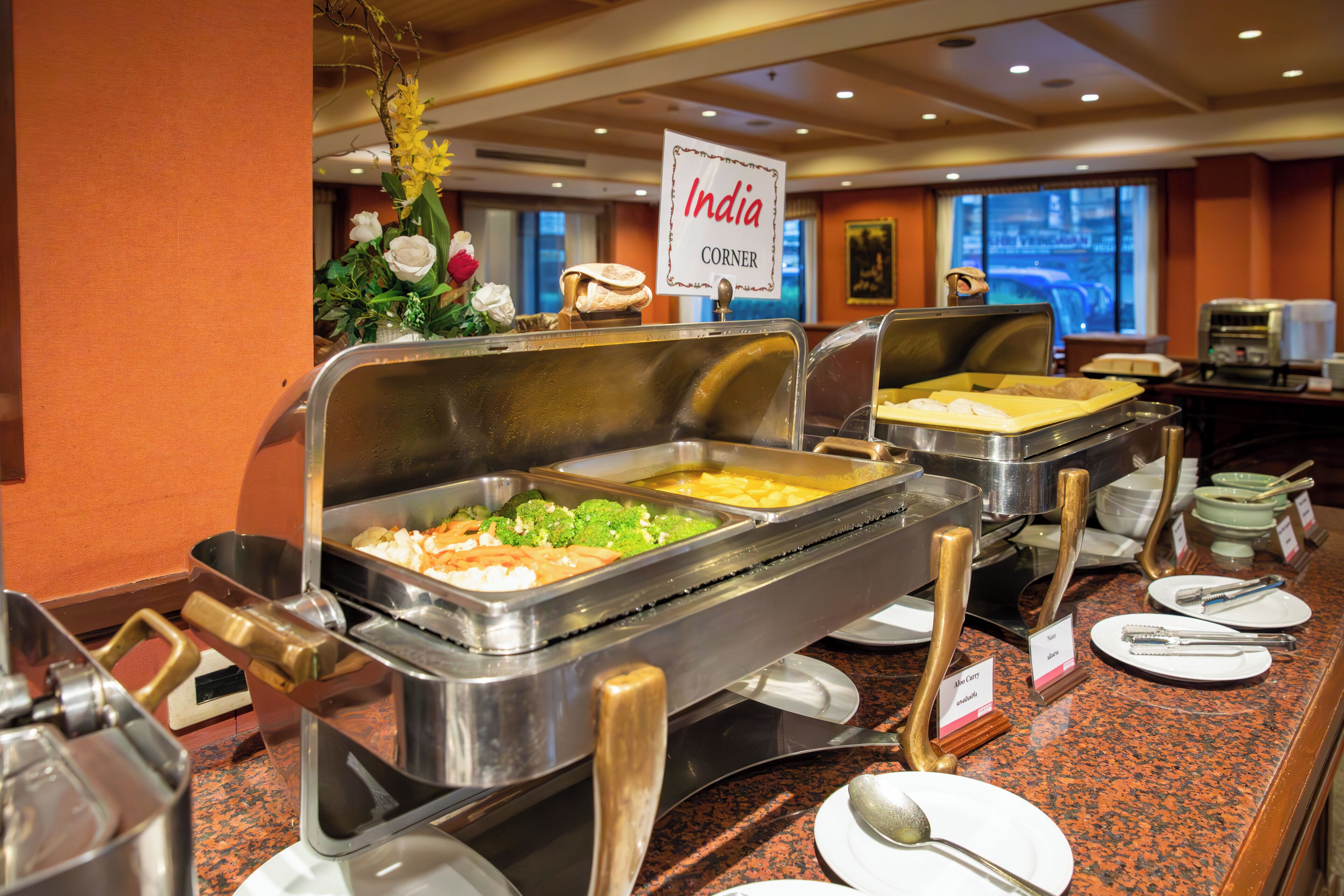 A buffet with various food options, a sign indicating 'India Corner', and a window with a view of the city.