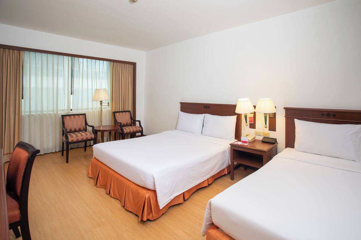 Habitación de hotel con dos camas, un escritorio, una silla y una lámpara.