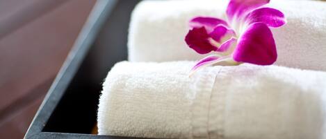 A wooden tray with two white towels and a purple orchid.