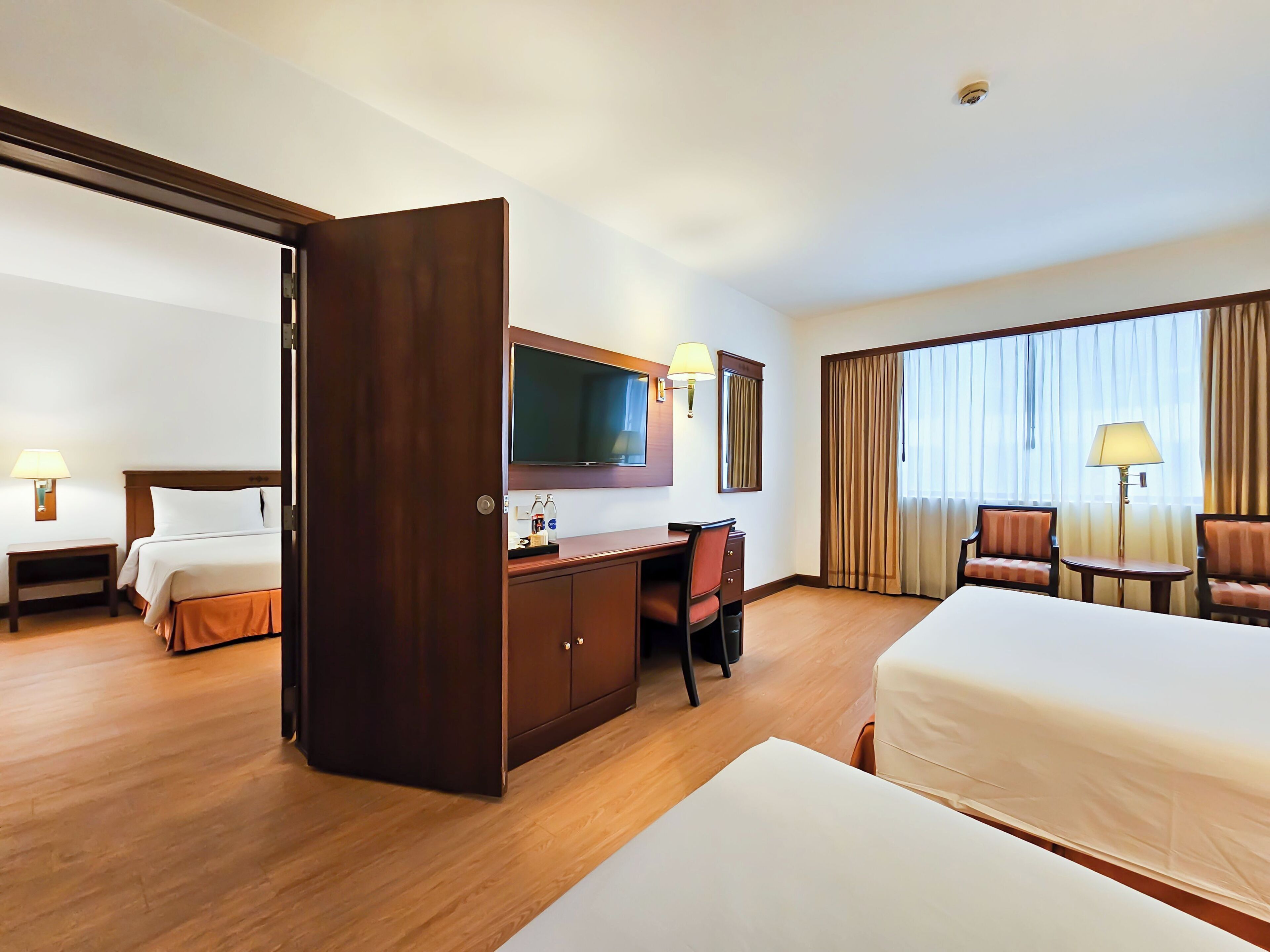 A hotel room with a bed, a desk, a chair, a TV, and a window with curtains.