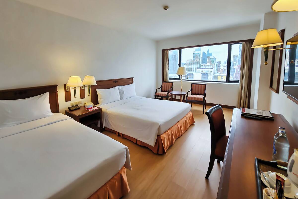 Habitación de hotel con dos camas, un escritorio, una silla y vistas a la ciudad.