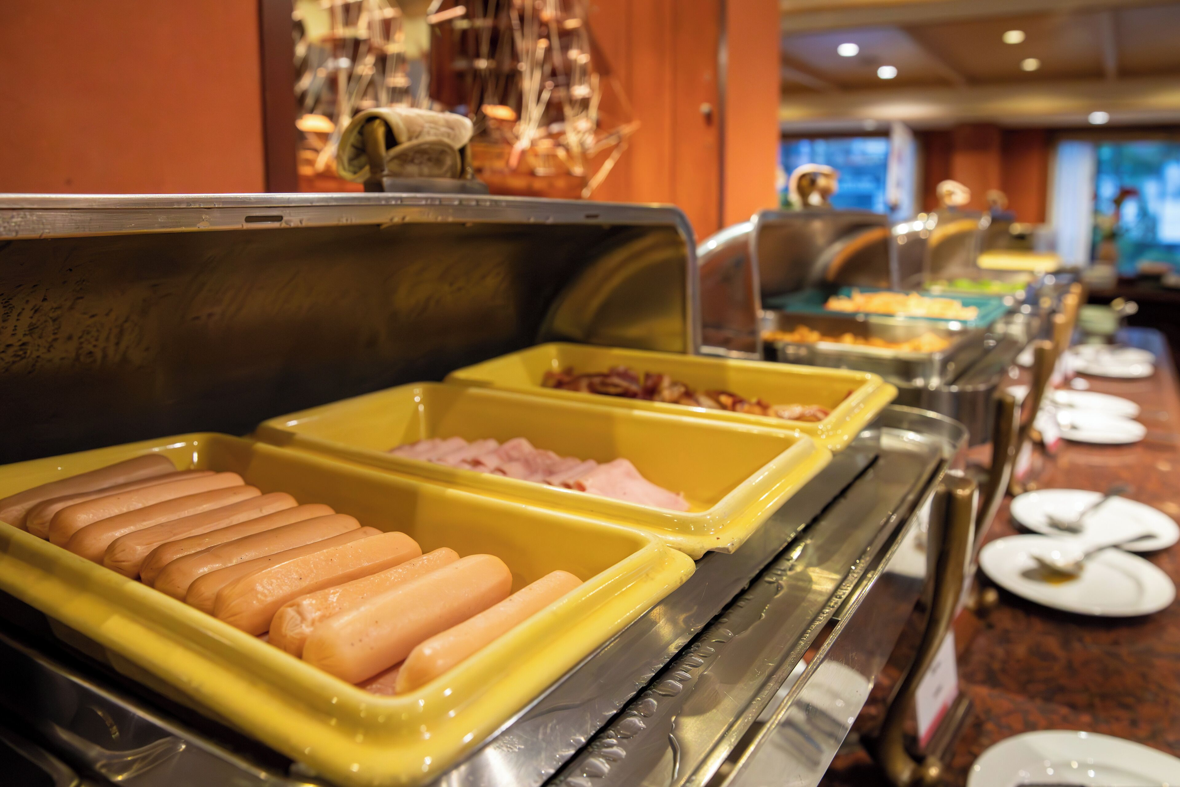 Een buffet met diverse gerechtjes, waaronder hotdogs en ham.