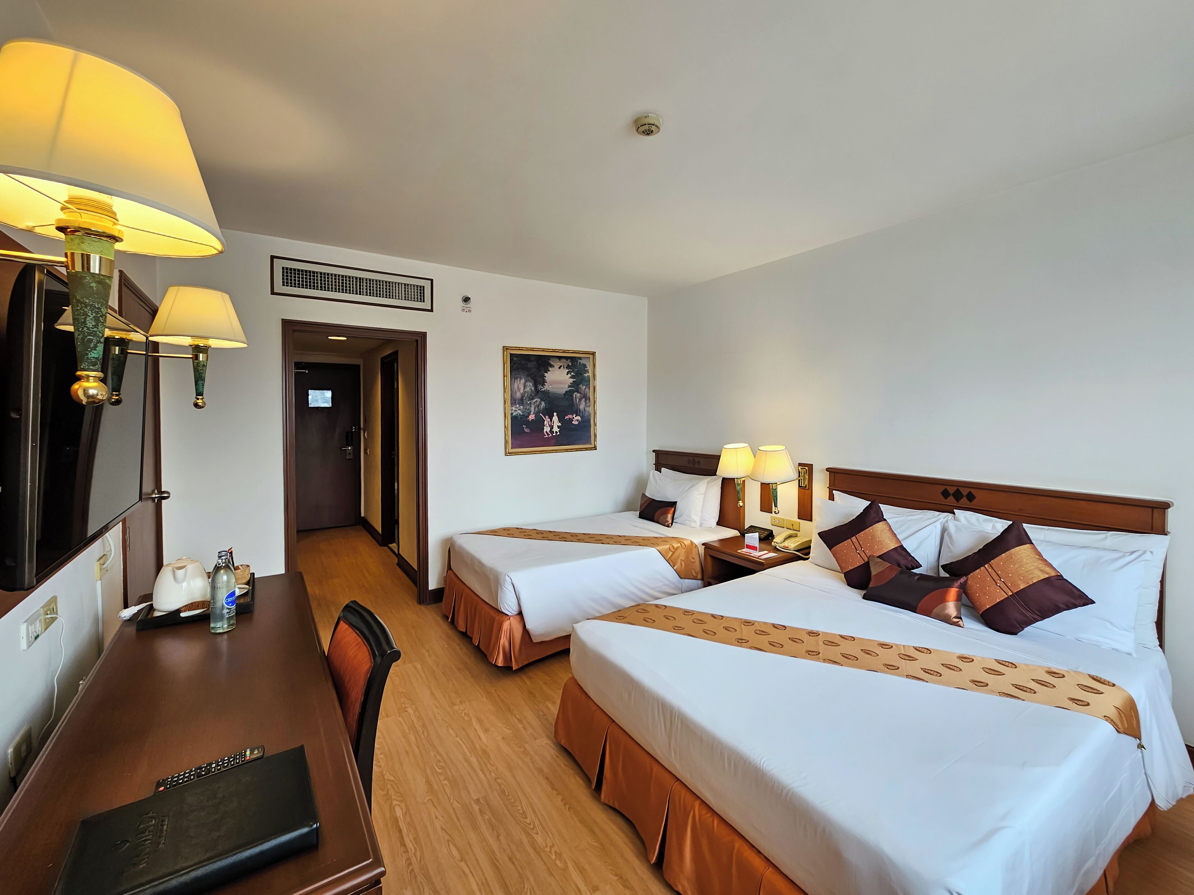 A hotel room with two beds, a desk with a computer, a chair, and a painting on the wall.