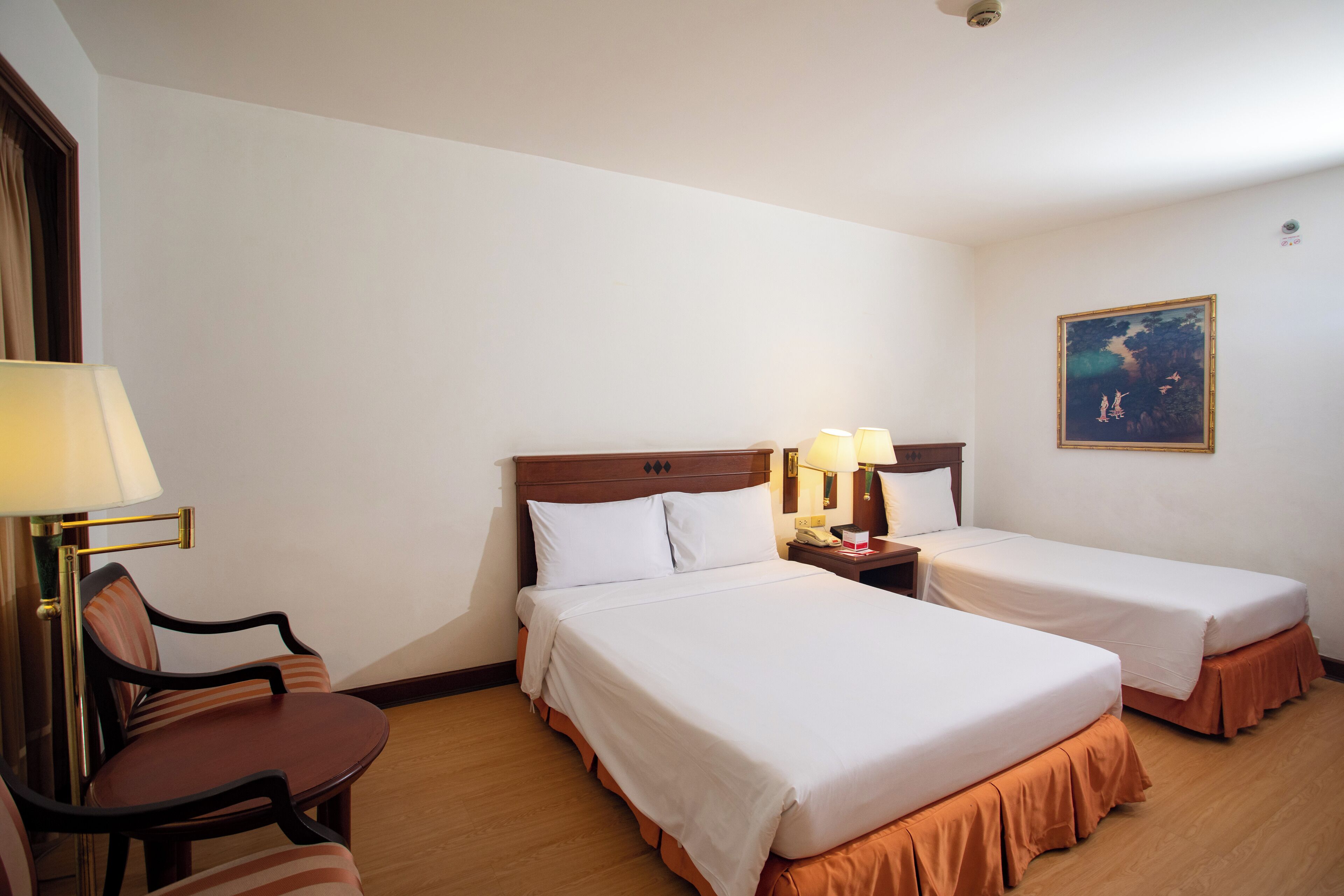 A hotel room with two single beds, a chair, a desk, and a nightstand with lamps.