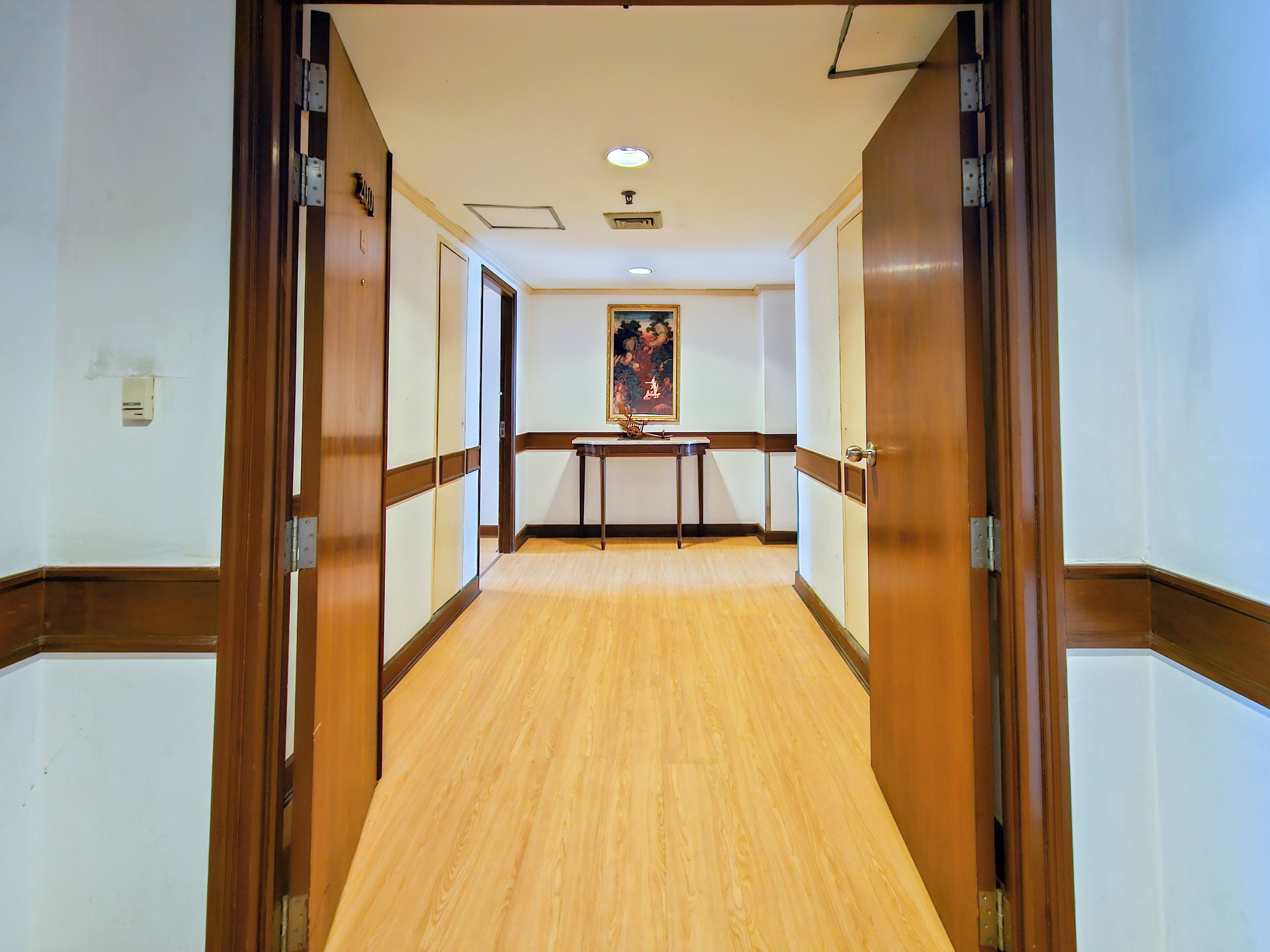 Un couloir d’hôtel avec un plancher en bois, un tableau accroché au mur et une table au bout.