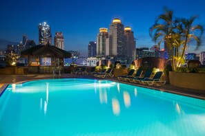 A rooftop pool with lounge chairs and a view of a city skyline at dusk. - Ramada D'MA Bangkok (Bangkok)