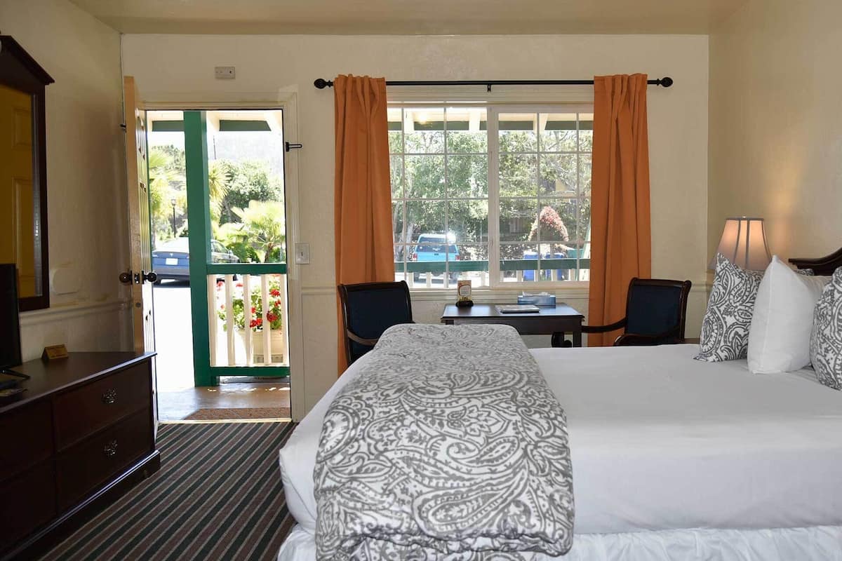 Une chambre d’hôtel avec un grand lit, un bureau, deux chaises, une commode et une fenêtre avec des rideaux.