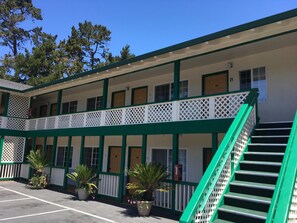A motel with a two-story structure, a covered outdoor area with a staircase, and potted plants.