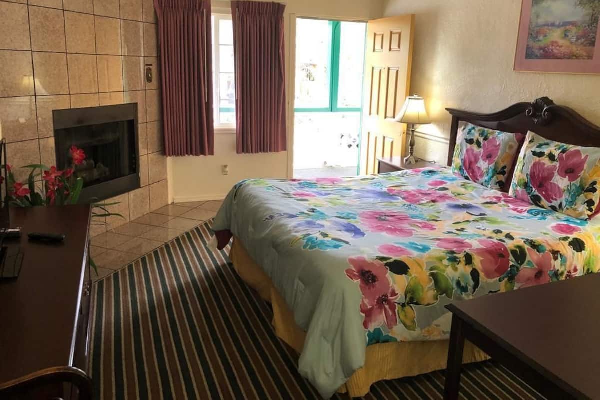 Une chambre d’hôtel avec un lit, une cheminée, un tapis à rayures, un bureau et une porte donnant sur l’extérieur.
