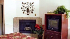 A bedroom with a bed, a fireplace, a television, and a decorative wall piece.