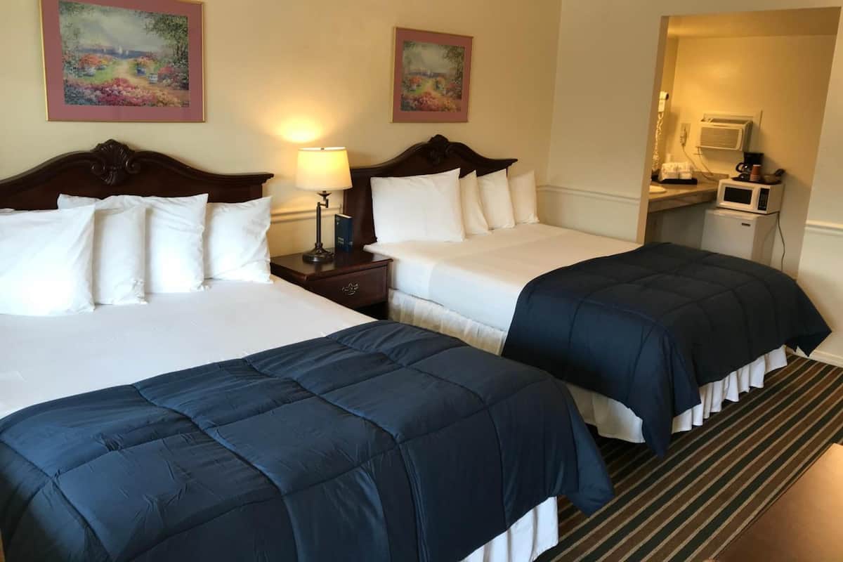 Une chambre d’hôtel avec deux lits, une table de chevet avec une lampe, un four à micro-ondes et une petite kitchenette.
