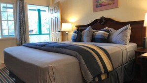 A neatly made bed with striped bedding, a wooden headboard, and a bedside lamp.