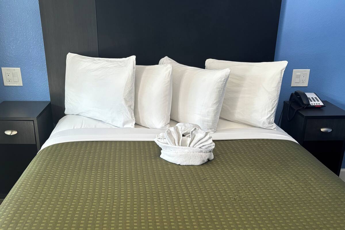 A neatly made bed with a green patterned bedspread, white pillows, and a folded towel on the bed.